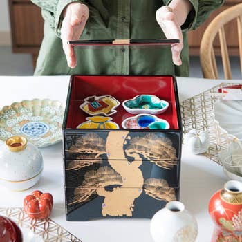 person opening the black bento box with a gold pine tree illustrated on it 