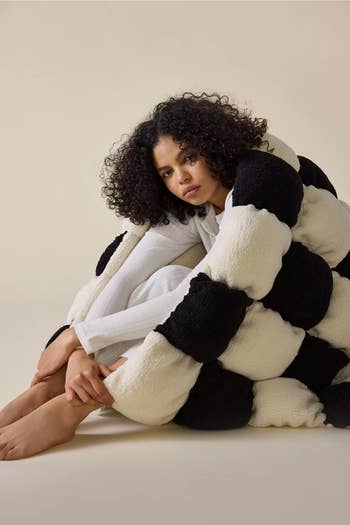 Person wrapped successful  a large, textured, checkered blanket, sitting connected  the floor. The country   conveys warmth and coziness, suitable for a buying  feature