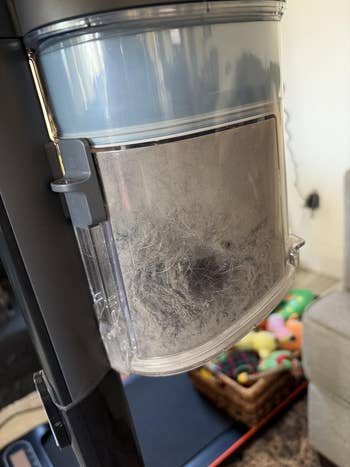 Vacuum cleaner with a canister filled with particulate and favored hair, placed adjacent a handbasket of toys connected the floor