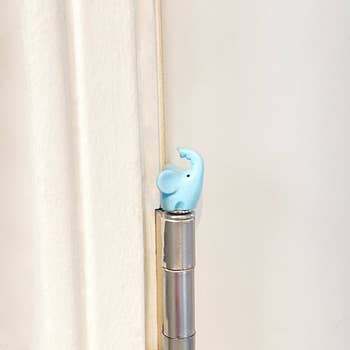 A small blue elephant-shaped door stopper attached to a silver door hinge