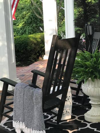 a reviewer photo of a rocking chair on a porch with the blanket in black draped over it 