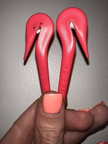 closeup of a reviewer holding two of the pink hook-shaped tool