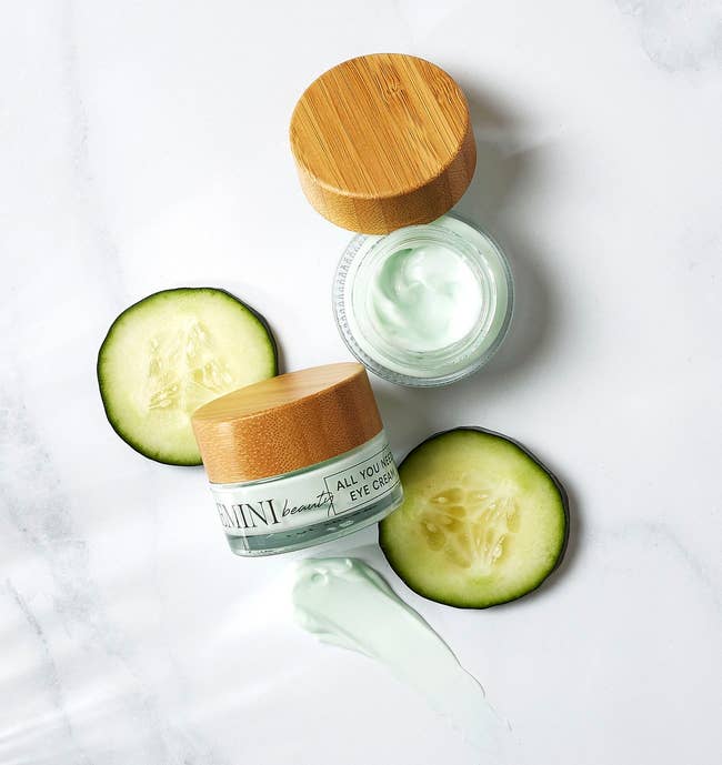 two tubs of light green eye cream with two slices of cucumber and a product swatch next to them