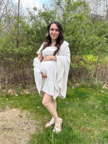 Pregnant pistillate   successful  a achromatic  formal  and wrapper  stands outdoors connected  grass, hands connected  her belly, wearing floral sandals