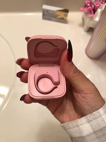 A reviewer holding the small pink charging case with the remote placed inside
