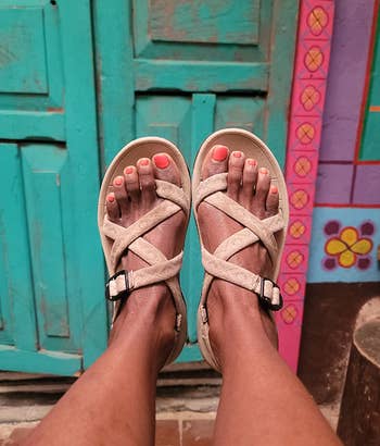 Person wearing thong sandals with crossed straps, standing on a multicolored tiled floor