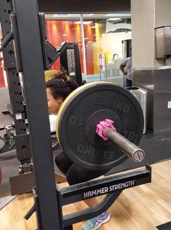 reviewer pic of reviewer squatting with barbell loaded with plates held in place by pink barbell clamp