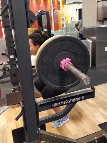 reviewer pic of reviewer squatting with barbell loaded with plates held in place by pink barbell clamp