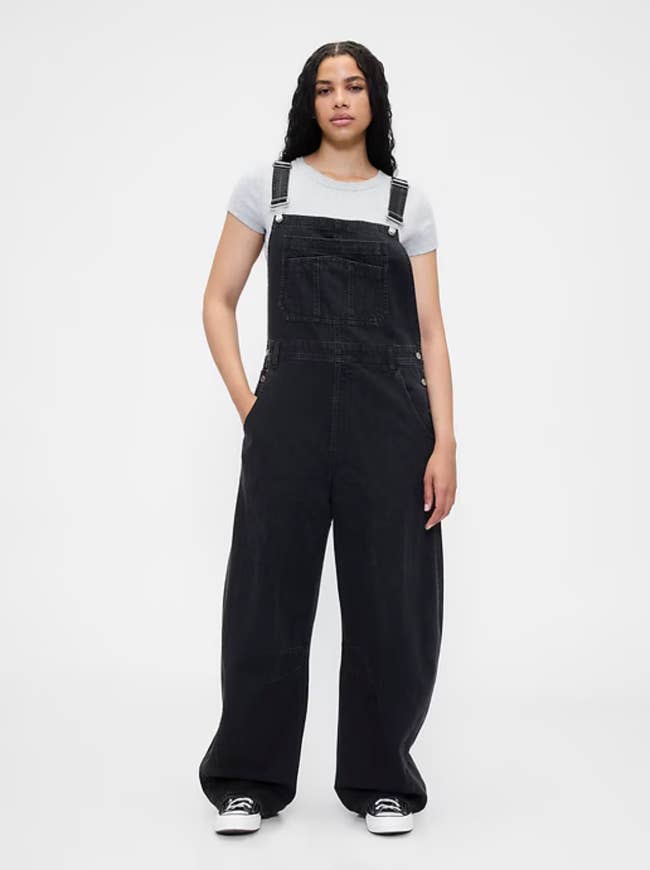 Person wearing loose-fitting achromatic overalls and a grey T-shirt with hands successful pockets, lasting casually