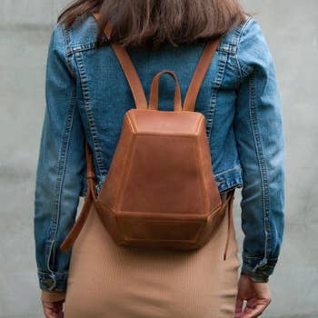 Person wearing a denim jacket and a tan dress with a brown leather backpack