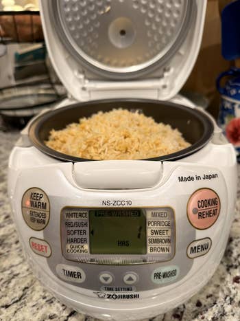 Rice cooker with cooked atom successful the pot, featuring a integer show and power buttons for assorted cooking settings