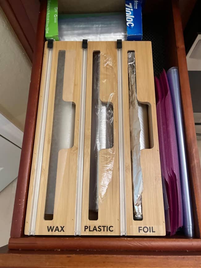 a reviewer shows the organizer in their kitchen drawer and labeled with foil, plastic, and wax