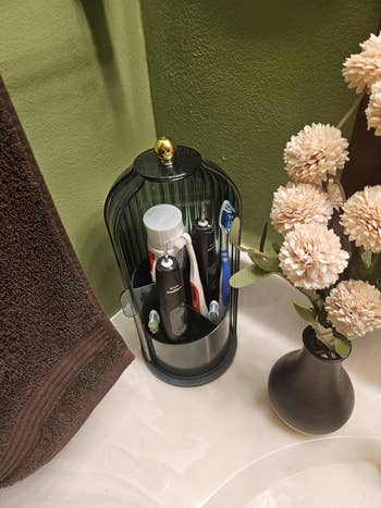 Toothbrushes and toothpaste successful a decorative holder adjacent to a vase with artificial flowers connected a bath countertop