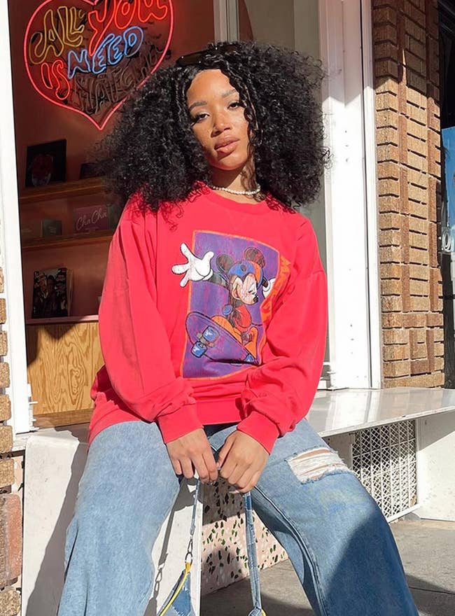 a model in a red long sleeve sweatshirt with a graphic of mickey skateboarding on it