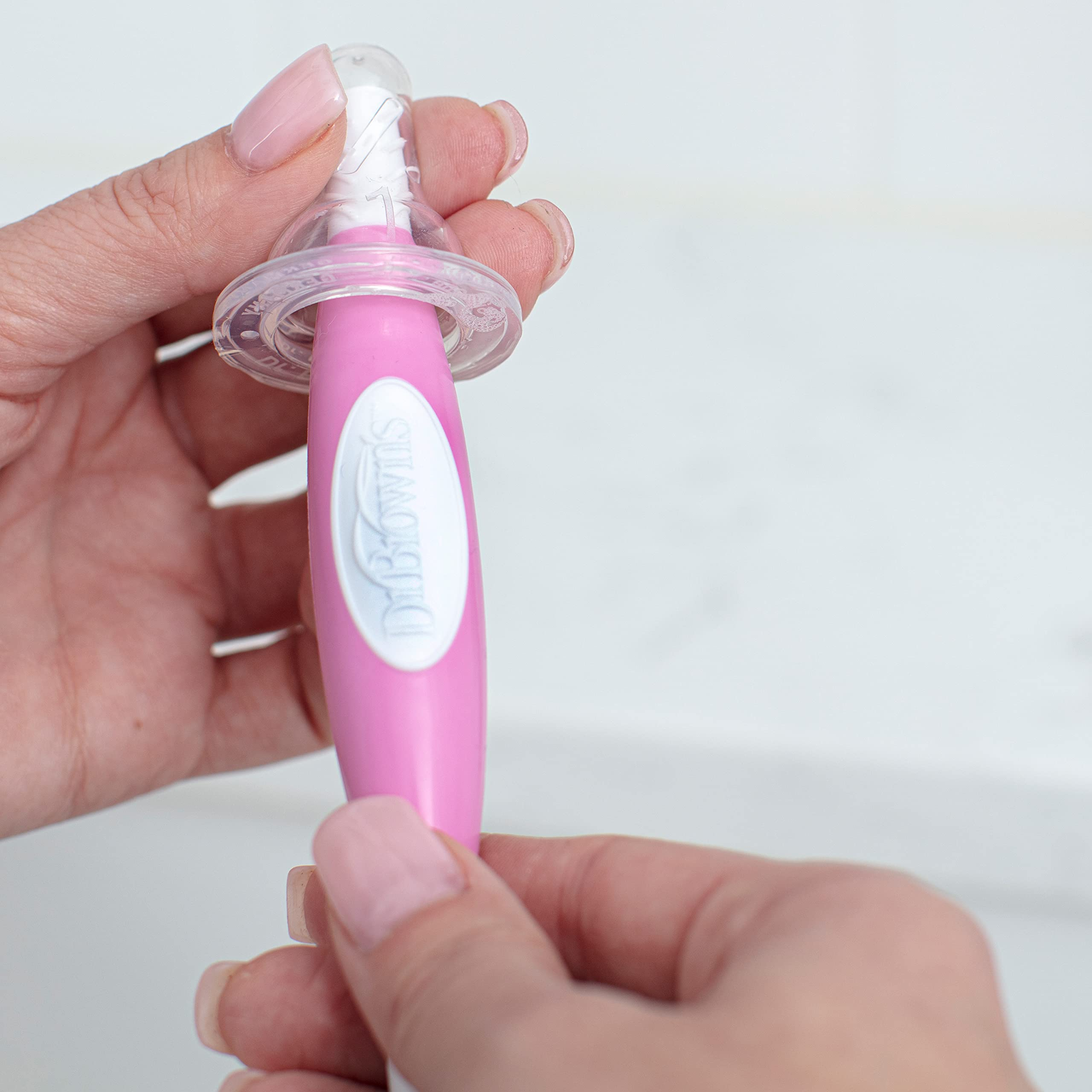 Person holding Dr. Brown's pinkish  babe  pacifier, showcasing the merchandise  design