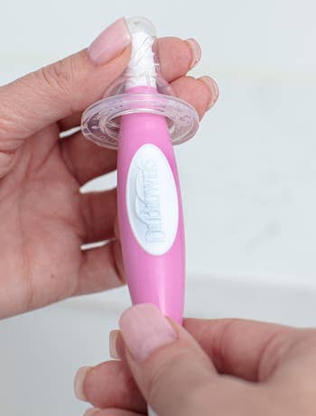 Person holding Dr. Brown's pinkish babe pacifier, showcasing the merchandise design