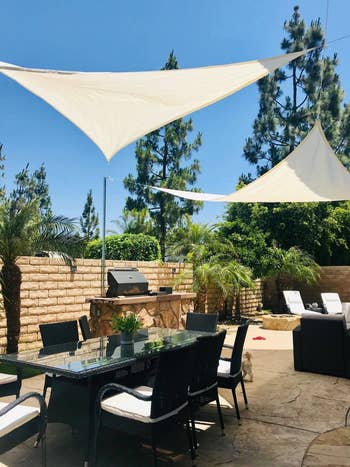 Outdoor patio with eating  table, chairs, grill, and achromatic  shadiness  sails. Lounge chairs and greenery successful  the background. Ideal for outdoor gatherings