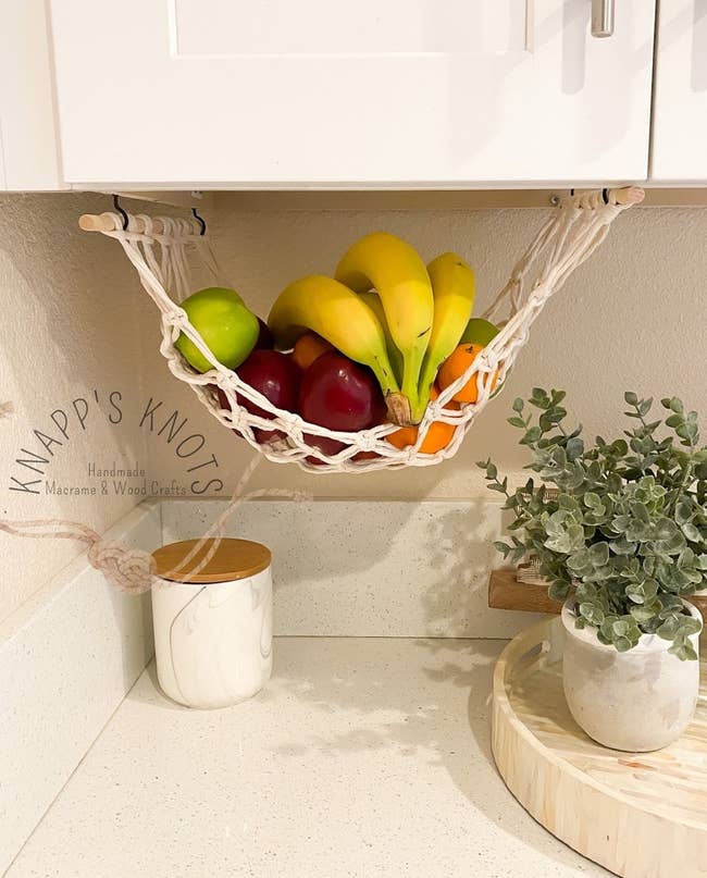 the white macrame hammock hanging under a cabinet with fruit inside