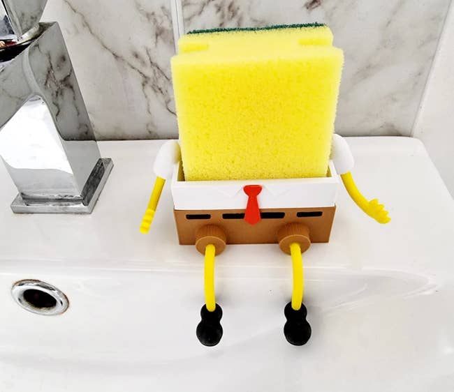 A spongeBob sponge holder on a sink holding a yellow sponge