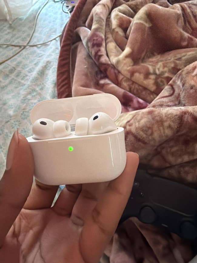 Hand holding wireless earbuds lawsuit  with earbuds inside, placed connected  a patterned broad  background, highlighting portable audio tech