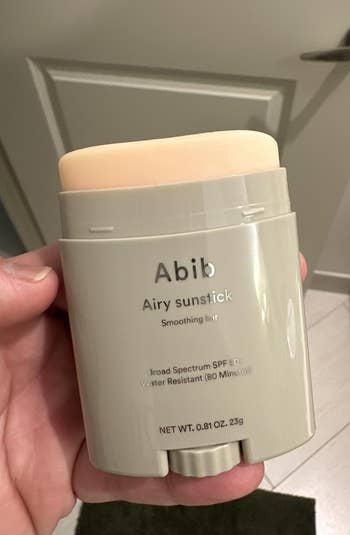 Hand holding Abib Airy Sunstick with SPF 50+, water-resistant for 80 minutes, successful beforehand of a door