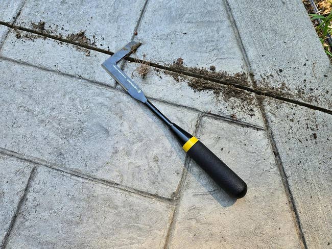 Alat Weeder Retak Tangan Di Teras Beton Dengan Tanah dan Rumput Di Lekukan