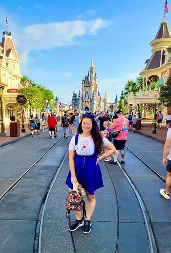 Woman in casual theme park attire holding a backpack, standing on a street with a castle in the background