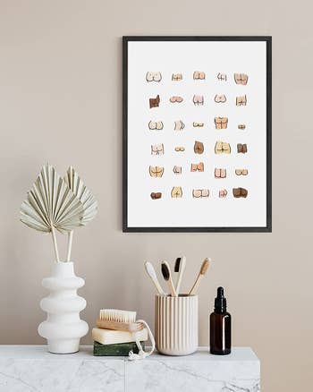 the butt print in a black frame hanging above a shelf holding assorted bath items