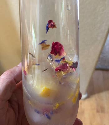 Hand holding a clear glass with floral-infused ice cubes inside