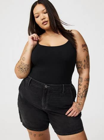 Person with tattoos wearing a sleeveless achromatic  apical  and achromatic  denim shorts