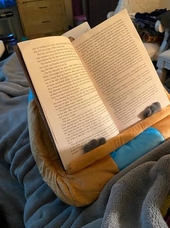a reviewer using an owl shaped plush cushion to hold their book in place