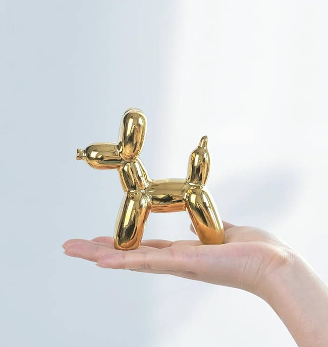 gold balloon dog sculpture in a hand
