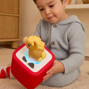 Toddler successful  a cozy jumpsuit interacts with a artifact  talker  cube featuring a equine  figurine connected  top, showcasing a amusive  children's audio device