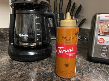 Torani Pumpkin Pie Puremade Sauce bottle on a kitchen counter, placed between a coffee maker and a toaster