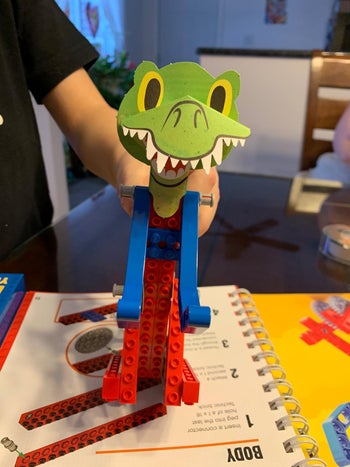 Reviewer holding up a dinosaur they made on top of the instruction book
