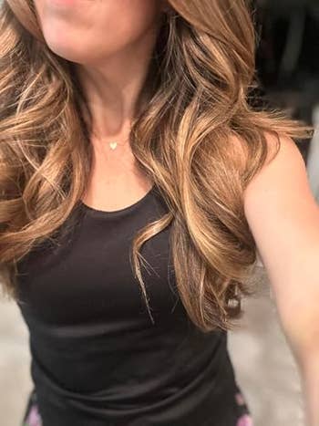 Person with styled wavy hairsbreadth wearing a sleeveless apical and a heart-shaped necklace, pictured from the shoulders down