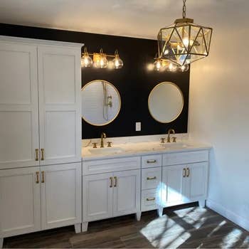 Modern bathroom with double vanity, gold fixtures, twin mirrors, geometric pendant light, and wooden flooring
