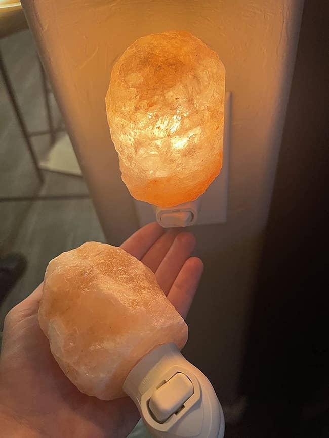 reviewer photo of them holding an unlit rock salt nightlight in front of a lit one plugged into their wall