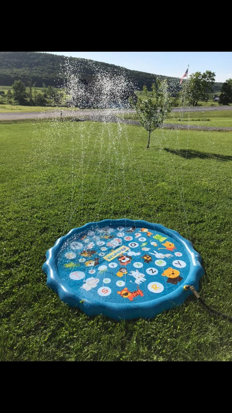 A round children's splash pad on a grassy lawn, spraying water