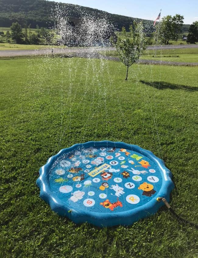 A round children's splash pad on a grassy lawn, spraying water