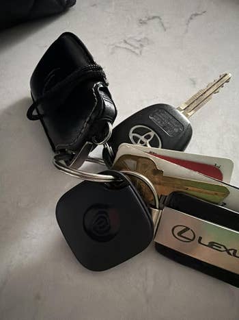 Keychain with car keys, a integer tracker, and assorted loyalty cards attached, including a Lexus paper and a achromatic pouch