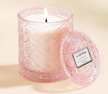 Scented candle by La Jolie Muse with lit wick, encased in a textured glass container