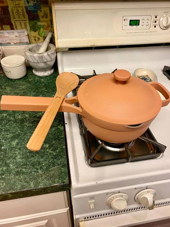 a closed pale pink sauce pot with a wooden spoon resting on the handle 