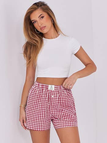 model successful  a fitted achromatic  harvest  apical  and reddish  checkered shorts poses against a neutral backdrop, showcasing casual manner  attire