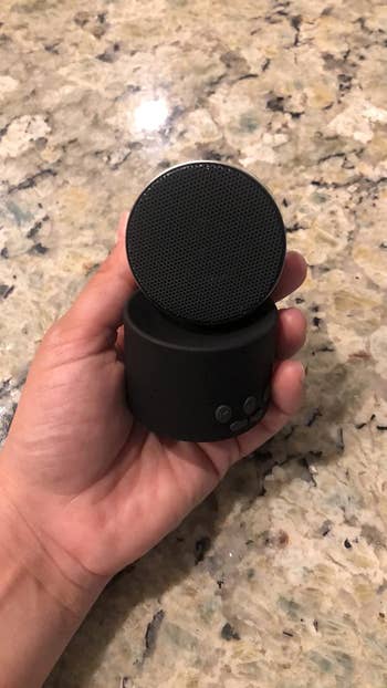 reviewer holding black and grey tiny sound machine and showing the speaker