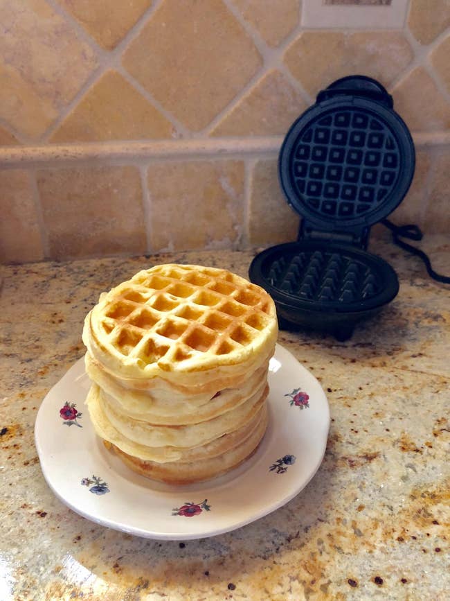 reviewer photo of a stack of waffles plus the mini waffle maker in the background