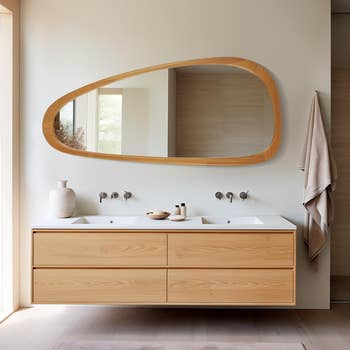 A modern bathroom vanity with a large oval mirror and dual sinks, accompanied by a simple vase