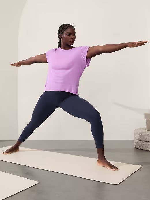 Person doing a yoga pose in a pastel top and dark leggings, for a shopping article on activewear