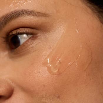 A close-up of a person's cheek with a clear skincare serum applied, emphasizing skin texture and sheen