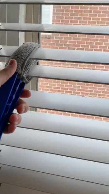 Reviewer using three pronged duster to squeeze dust off a window shade 